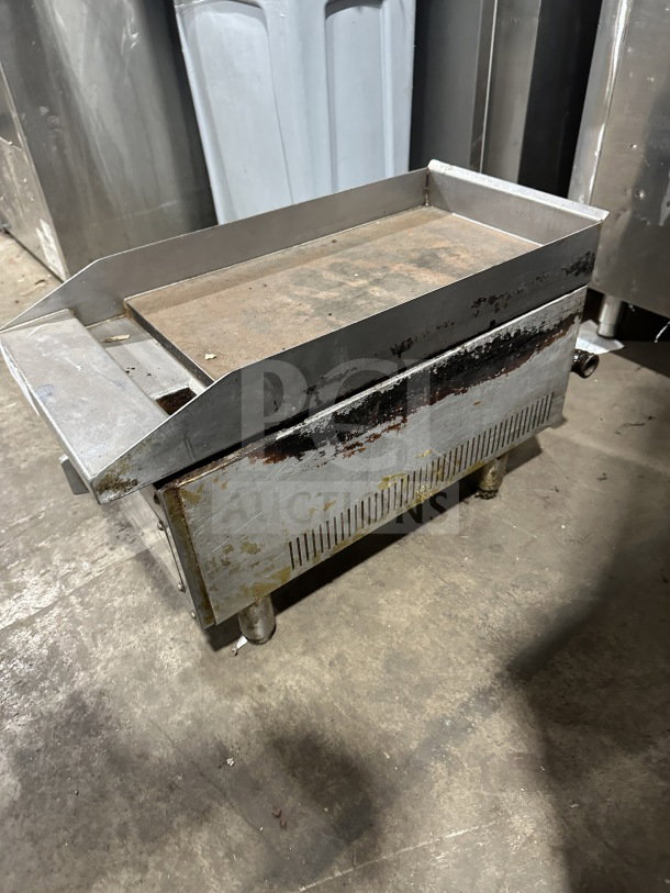 Commercial stainless steel gas-powered countertop flat top griddle on legs, showing signs of wear.