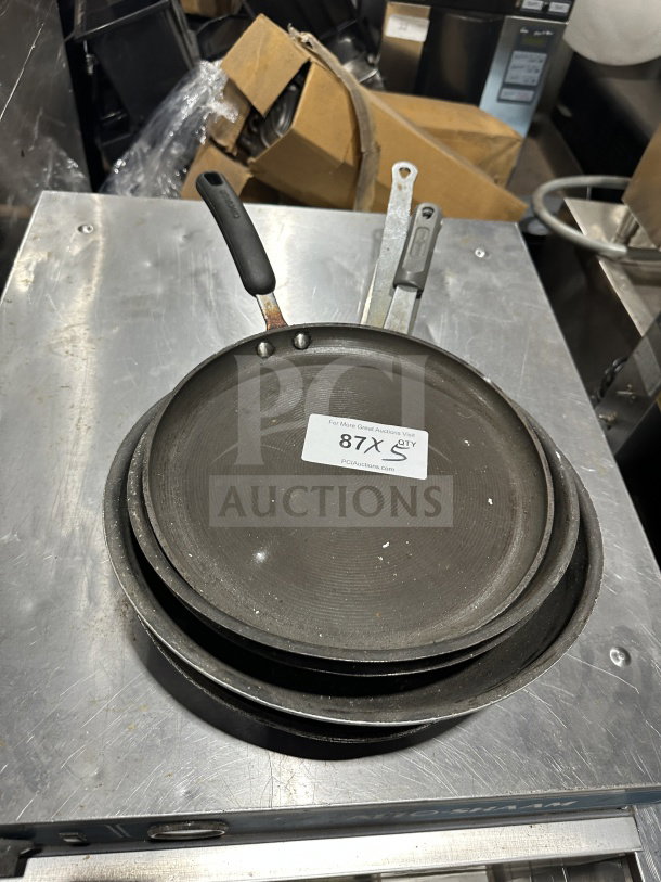 Commercial stainless steel non-stick fry/griddle pan set, used condition, stack of three pans, black handle grips, visible label.