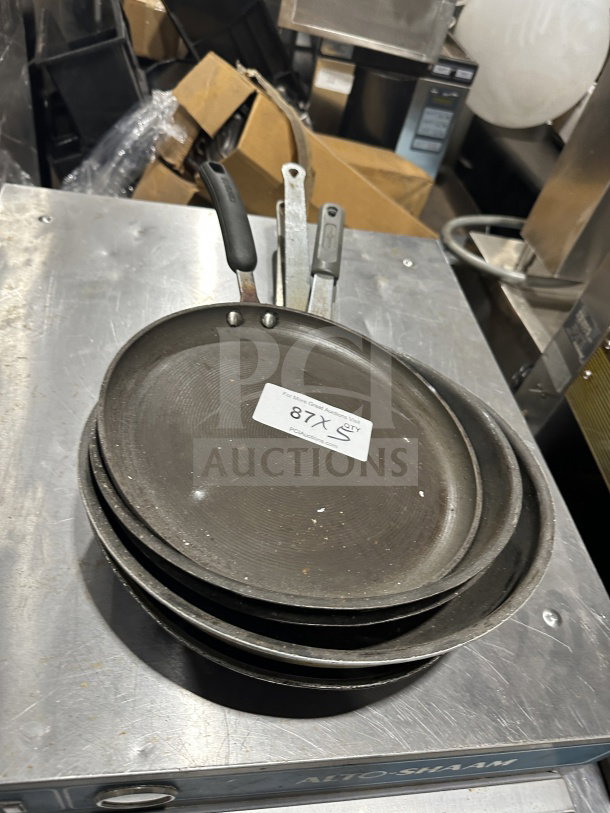 Set of commercial stainless steel non-stick fry/griddle pans, moderate wear, three pans in stack, auction tag "87X".