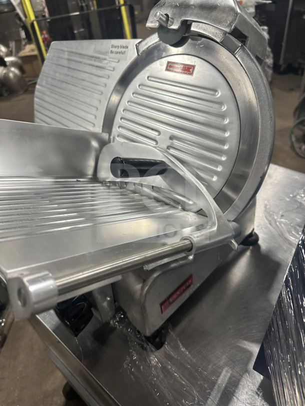Avantco 300ES12 stainless steel deli slicer, 12" semi-automatic, on legs, 110/120V, sharp blade warning label visible.