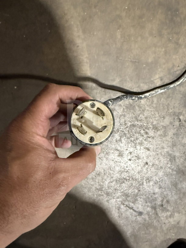 Hand holding a plug for a commercial stainless steel electric conical dough rounder machine, showing prongs.