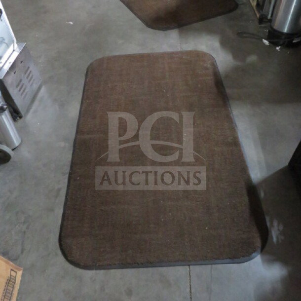 Brown 36x60 rug with rounded corners on concrete floor, showing a subtle checker pattern. Used condition.