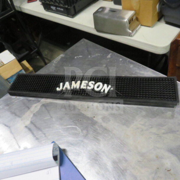 Jameson bar mat, black rubber with raised white logo, long rectangular shape, used condition, suitable for bar settings.