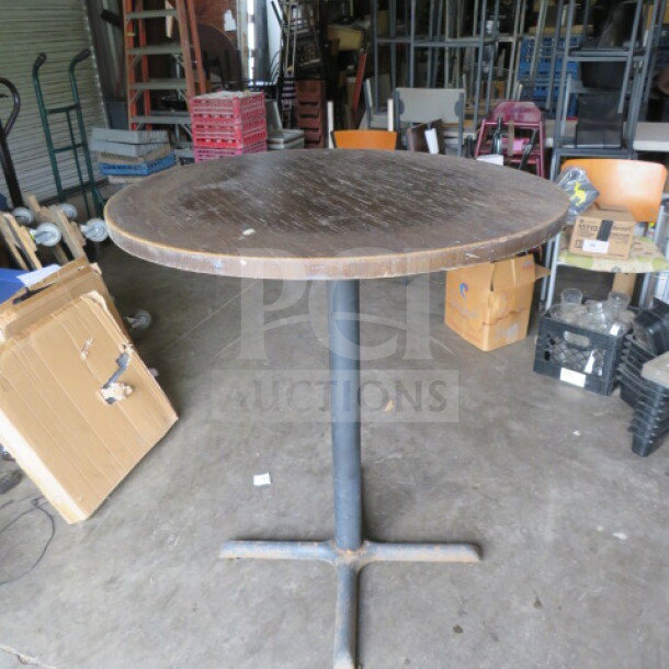 Round wooden table with a pedestal base, 36x30 inches. Rustic surface, metal base shows wear. Ideal for vintage decor.
