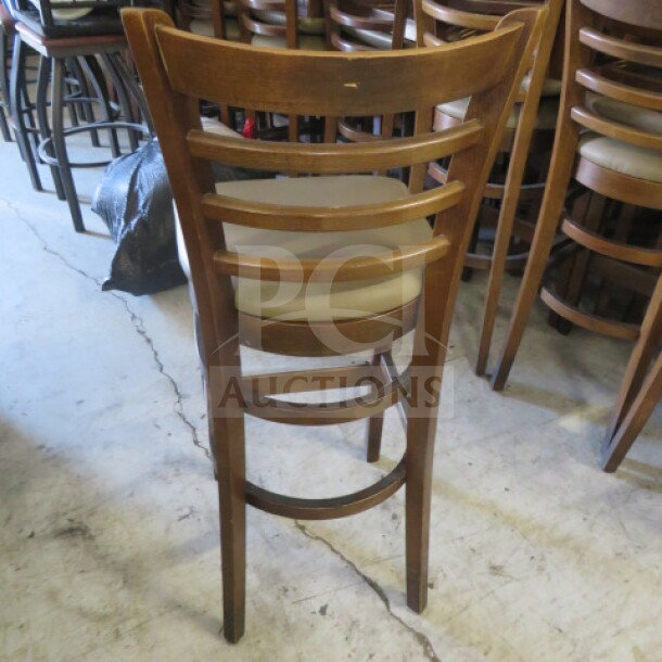 Wooden bar height chair with brown cushioned seat, ladder-back design. Slight wear, suitable for bar or kitchen use.