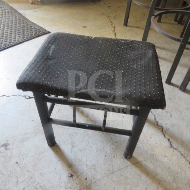 Black metal foot stool with cushioned seat, 18x16x16 inches. Minor wear visible, sturdy construction, ideal for added comfort.