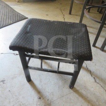 Black metal foot stool with cushioned seat, 18x16x16 inches. Minor wear visible, sturdy construction, ideal for added comfort.