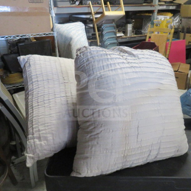 Two large, textured pillows in off-white fabric. Slightly worn condition. Set in a storage room.