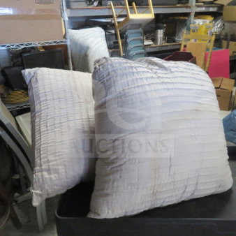 Two large, textured pillows in off-white fabric. Slightly worn condition. Set in a storage room.