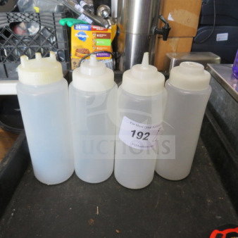 Assorted squeeze bottles with lids, four pieces, clear plastic, various lid styles, slight wear, auction tag "192" visible.
