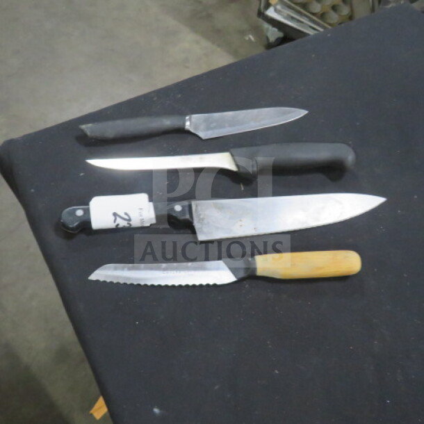 Assorted chef knives on black surface; includes serrated, paring, and chef's knife with various handle types.