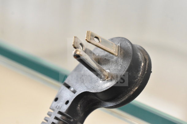 Close-up of a power plug from the stainless steel single door reach-in cooler, showing prongs and surface detail.