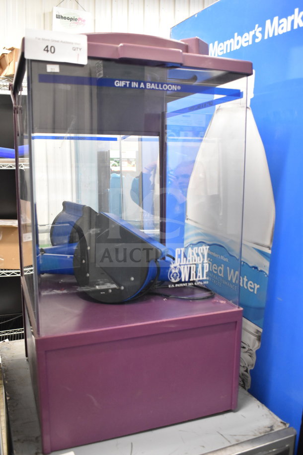 Countertop dry merchandising display case with a purple base and transparent sides. Features branding label "Gift in a Balloon."