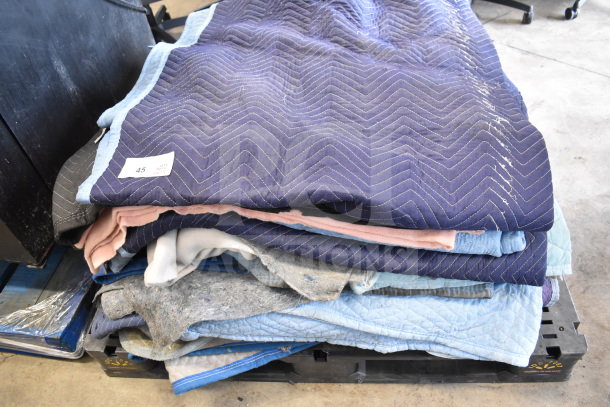 Stack of 15 moving blankets in various colors, neatly folded on a pallet. Some visible wear; perfect for protecting items during transit.