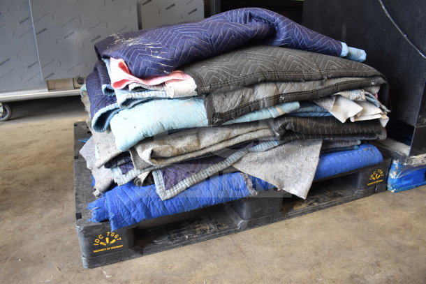 Stack of 15 moving blankets in various colors, lightly worn, on a pallet. Ideal for protecting items during transport.