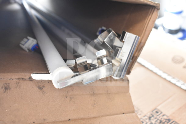 Cardboard box containing metal light fixture components, showing white tubes and clips, appearing new and unused.
