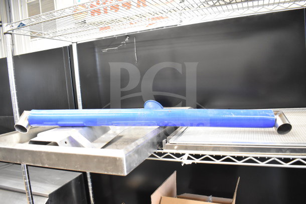 Metal panels and a blue cylindrical tube with angled ends are displayed on metal shelving. Industrial setting.