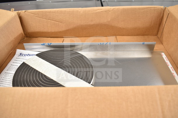 Cardboard box containing Scotsman ice machine part, instructions, and a metal piece; condition appears new.