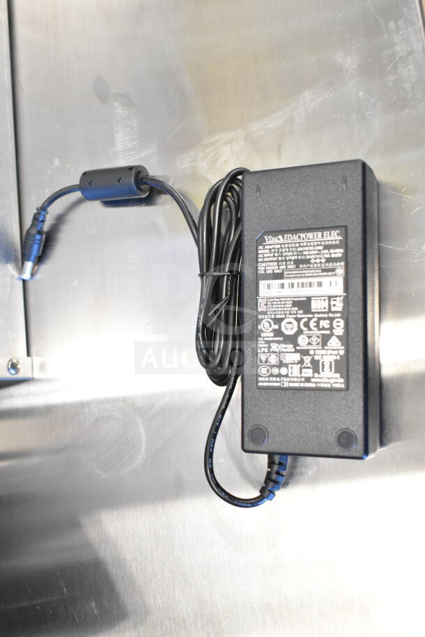 Power adapter for TSC TC210 label printer. Visible brand markings: Edacpower Elec. Black with attached cable.