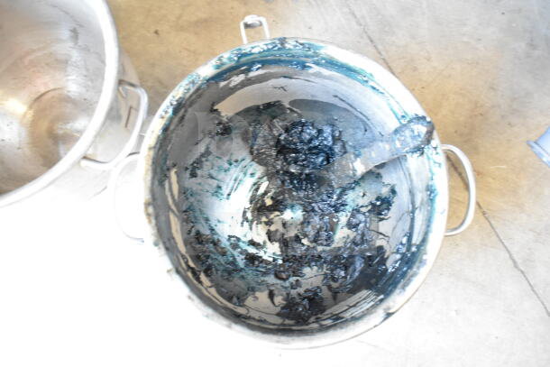 Two stainless steel mixing bowls with handles; one contains black residue and mixing tool, showing signs of use.