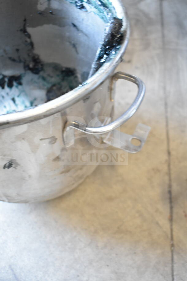 Stainless steel mixing bowl with handles, showing signs of use and remnants of material inside.