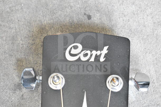 Cort guitar headstock with logo, chrome tuning pegs, visible wood grain, used condition showing slight wear.