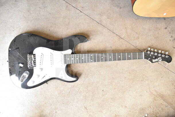 Black RockJam electric guitar, white pickguard, 6-string, in used condition with visible wear on body.