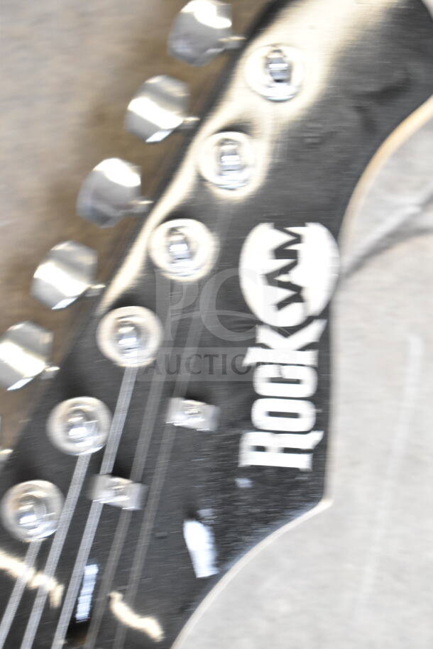 Close-up of the headstock of a RockJam guitar, featuring tuning pegs and partial logo visible. Condition appears used.