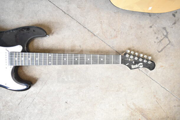 Two electric guitars, Cort and RockJam, on concrete floor. RockJam has a visible logo. Good condition.