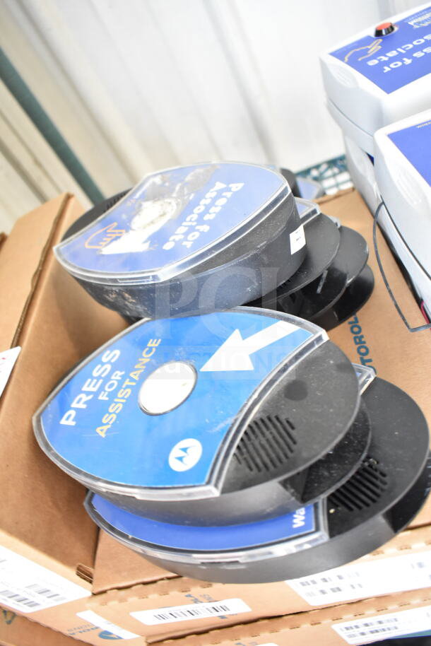 Stack of CB300-D Digital Callboxes on cardboard boxes, featuring "Press for Assistance" labels. Various items included.