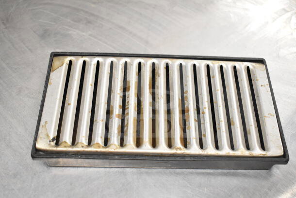 Metallic slotted tray with visible wear and discoloration, placed on a gray surface.