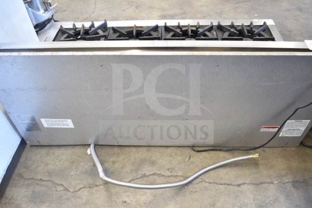 Wolf commercial 8-burner countertop gas range in metal finish. Features visible burner grates and attached gas line.