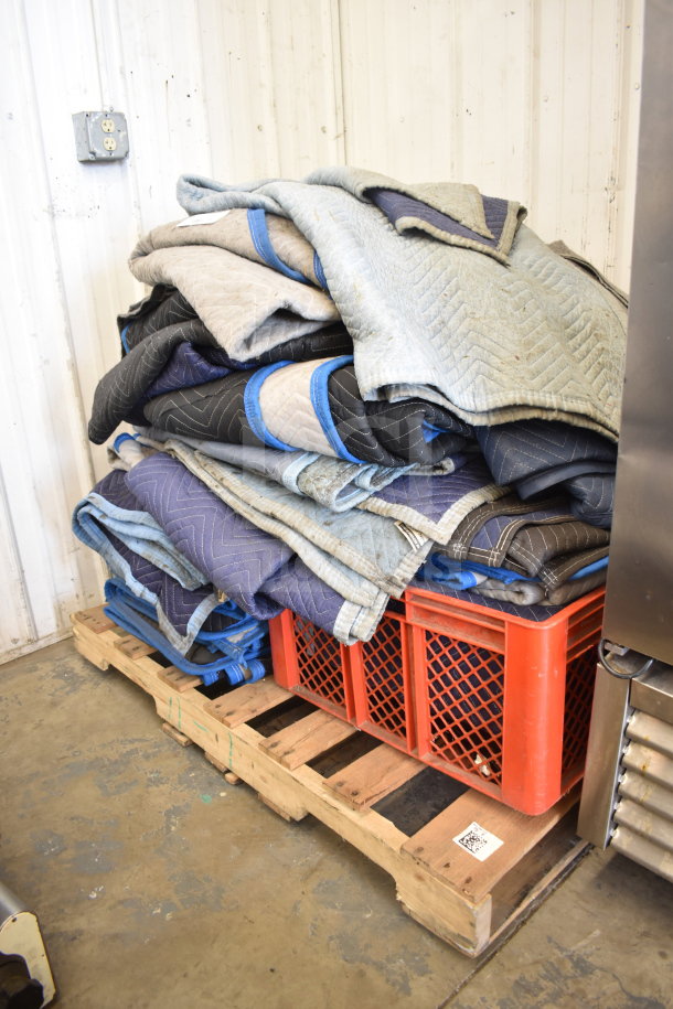 Stack of 14 moving blankets on a wooden pallet, assorted colors, with reinforced edges, slightly used condition.