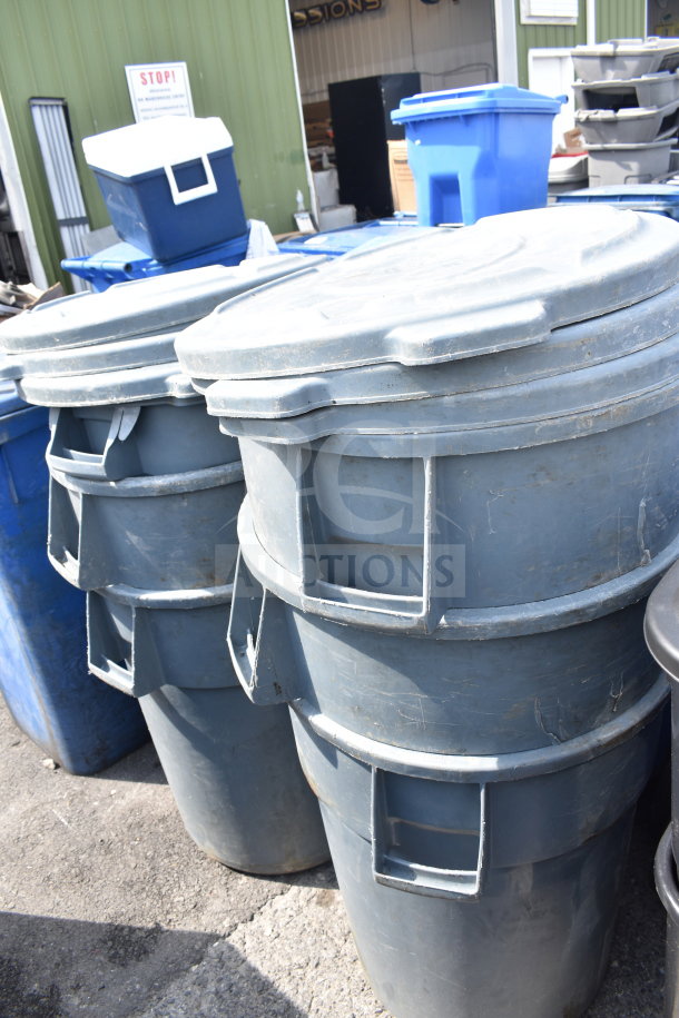 Six Rubbermaid Brute gray poly trash cans in used condition, stacked outdoors, showing durability and capacity.