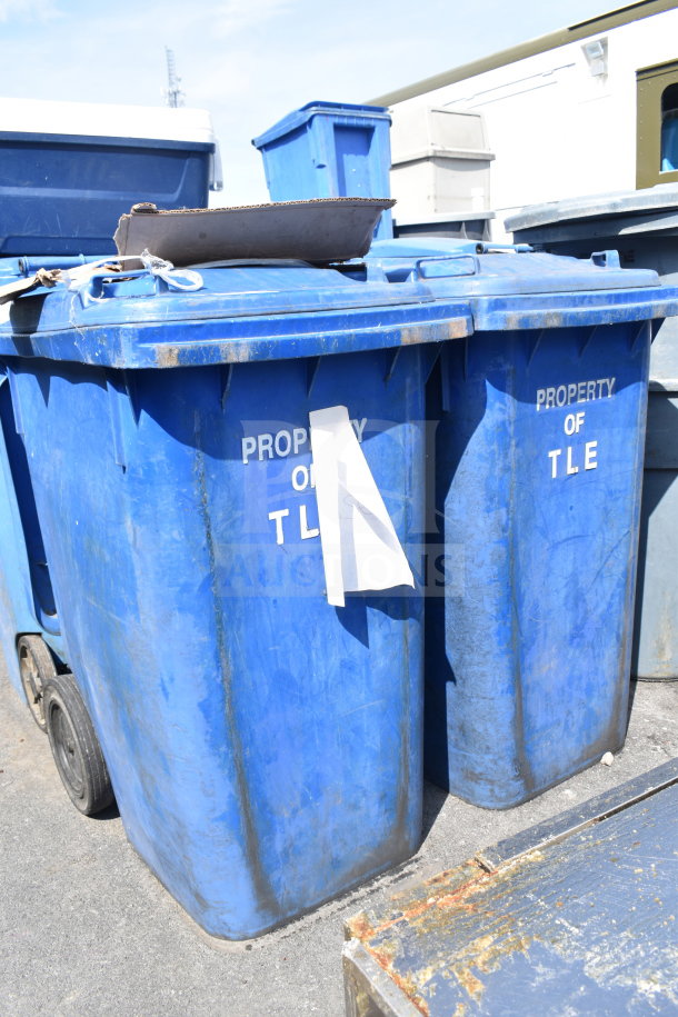 Two large blue poly trash cans labeled "Property of TLE," in used condition, with wheels for mobility.