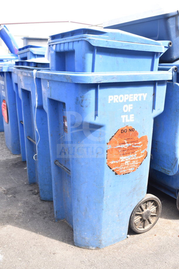 Three blue poly trash cans with wheels, "PROPERTY OF TLE" label, visible wear, auction includes 3 items.