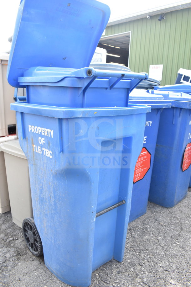 Three blue poly trash cans, marked "Property of TLE/TBC," with wheels and lids; weathered condition.