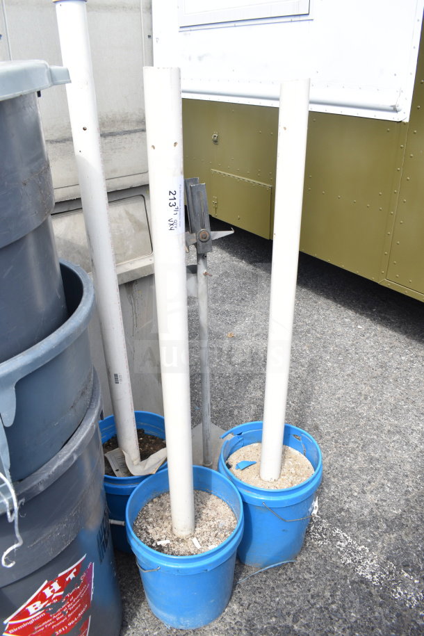 Four white poles in cement-filled blue bins, outdoor setting. Markings on one pole. Sold as 4 items per bid.