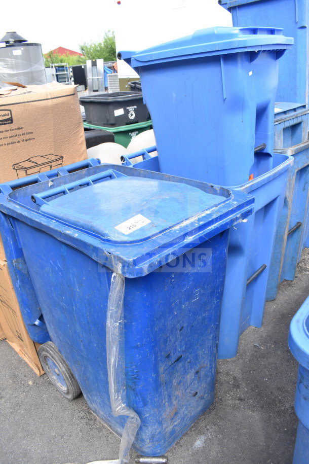 Four blue poly trash cans with lids, showing signs of wear. Includes "Property of" markings. Auction lot of four.