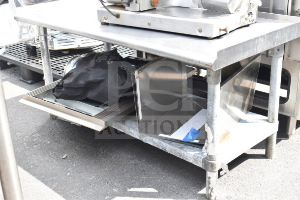 Metal table with under shelf containing baking pans and a black bag, in used condition.
