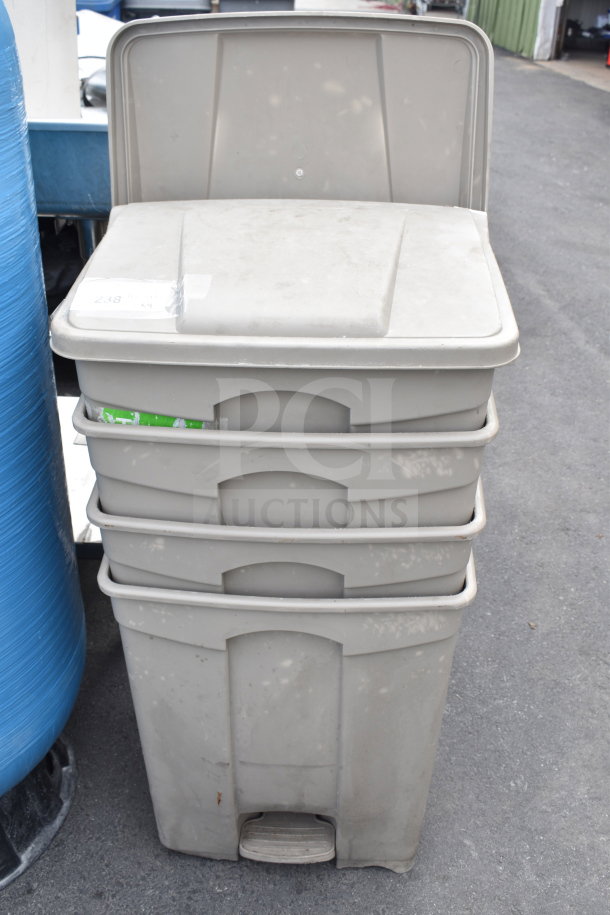 Four tan poly trash cans stacked, featuring pedal operation and visible wear. Ideal for bulk purchase auction.