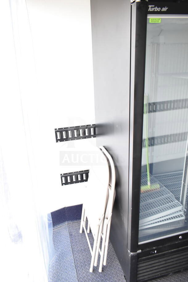 Alt text: 2020 Southern Dimensions 8.5x28 cold beverage/food trailer interior, featuring a Turbo Air cooler, folding chairs, and metal E-track system.