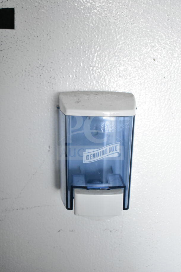 Wall-mounted Genuine Joe soap dispenser on white surface, featuring a transparent blue plastic reservoir and white push button.