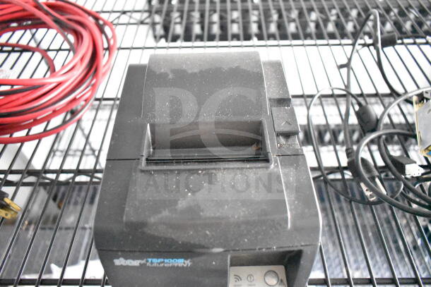 Star TSP100III receipt printer on a metal rack, dusty condition, accompanied by red cable.
