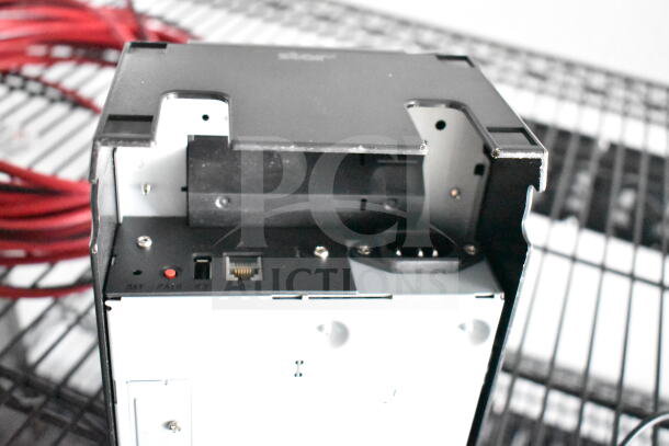 Rear view of a black and white electronic unit showing ports for connections and power supply on a metal rack.
