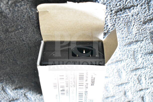 Power adapter by Zebra in open box, showing plug end. Box label details model and specifications.