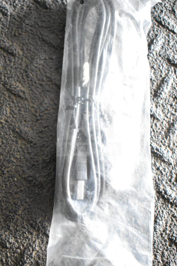 Vacuum-sealed black cable in transparent plastic packaging on a textured surface.