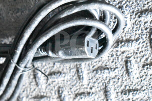 Coiled black electrical cord on textured surface, showing plug end. Condition appears used.
