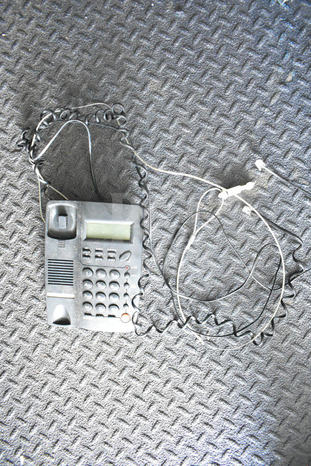 Rustic corded telephone on a textured dark floor, featuring a digital display and coiled cables.