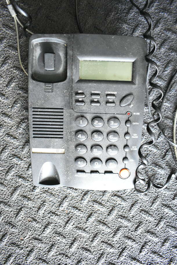 A black telephone with buttons, a small screen, and a coiled cord lies on a textured surface.